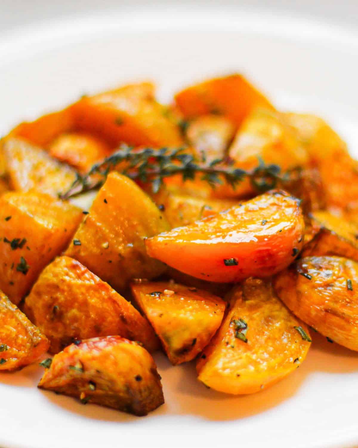 Roasted pieces of golden beets on a dish with a sprig of fresh thyme on top. 