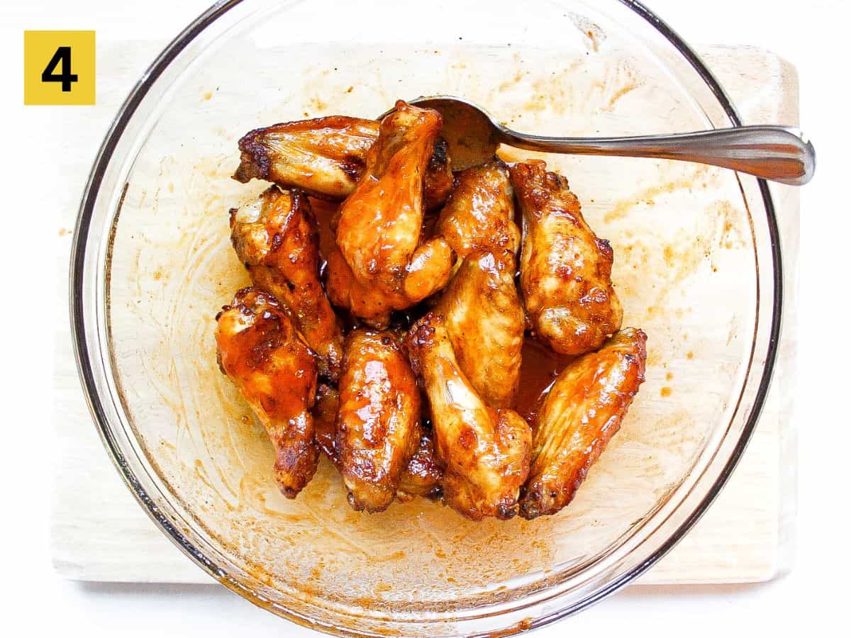 Chicken wings tossed in a buffalo sauce in a glass large bowl.