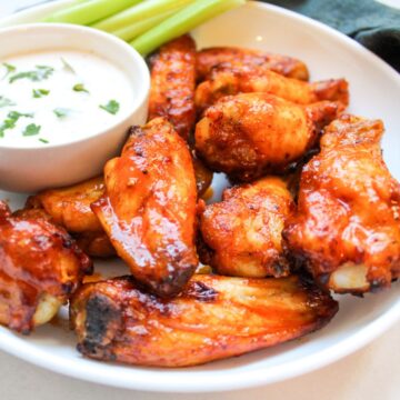 Buffalo chicken wings in a white dish with a side of blue cheese, celery and carrot sticks.