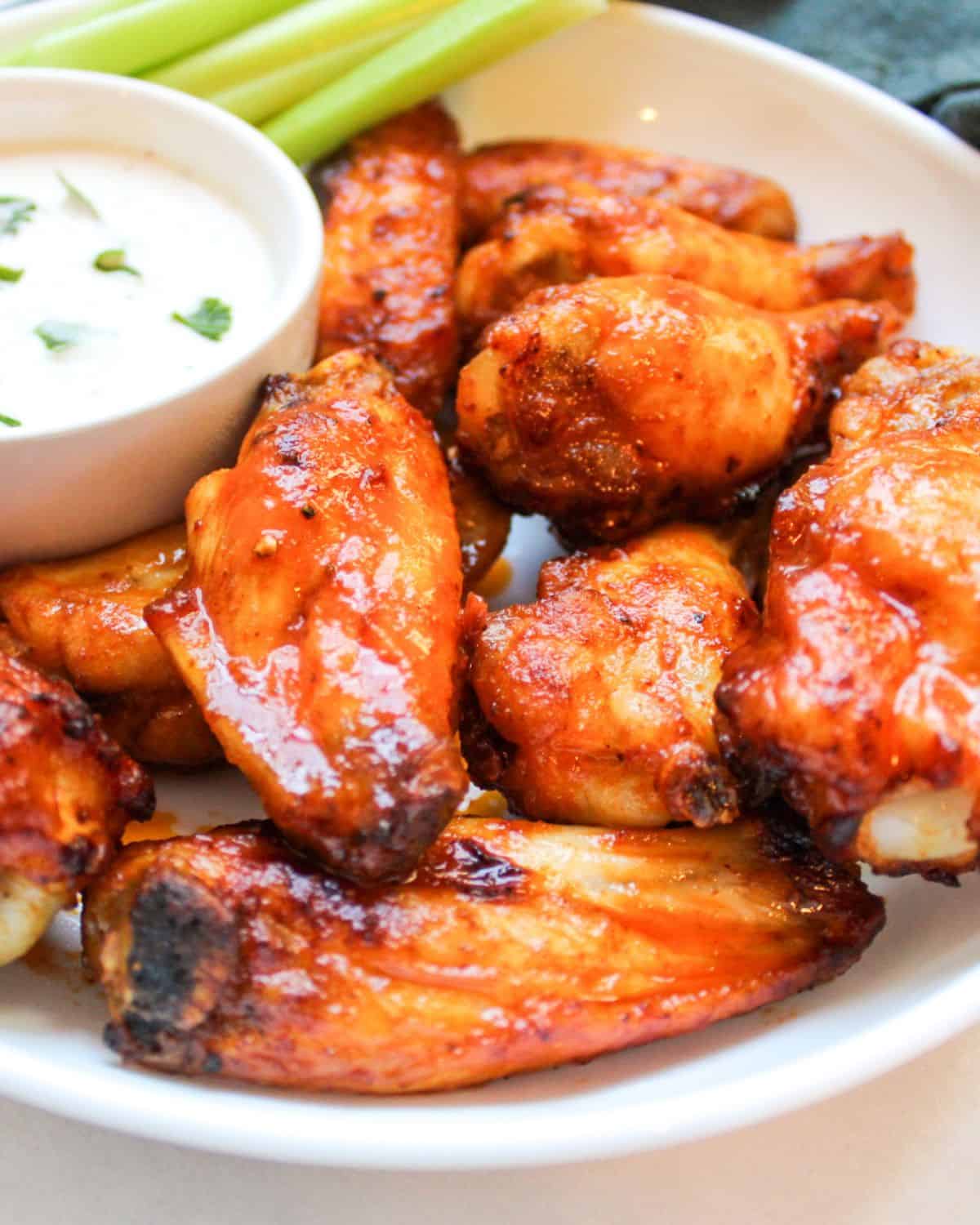 Buffalo chicken wings in a white dish with a side of blue cheese, celery and carrot sticks. 
