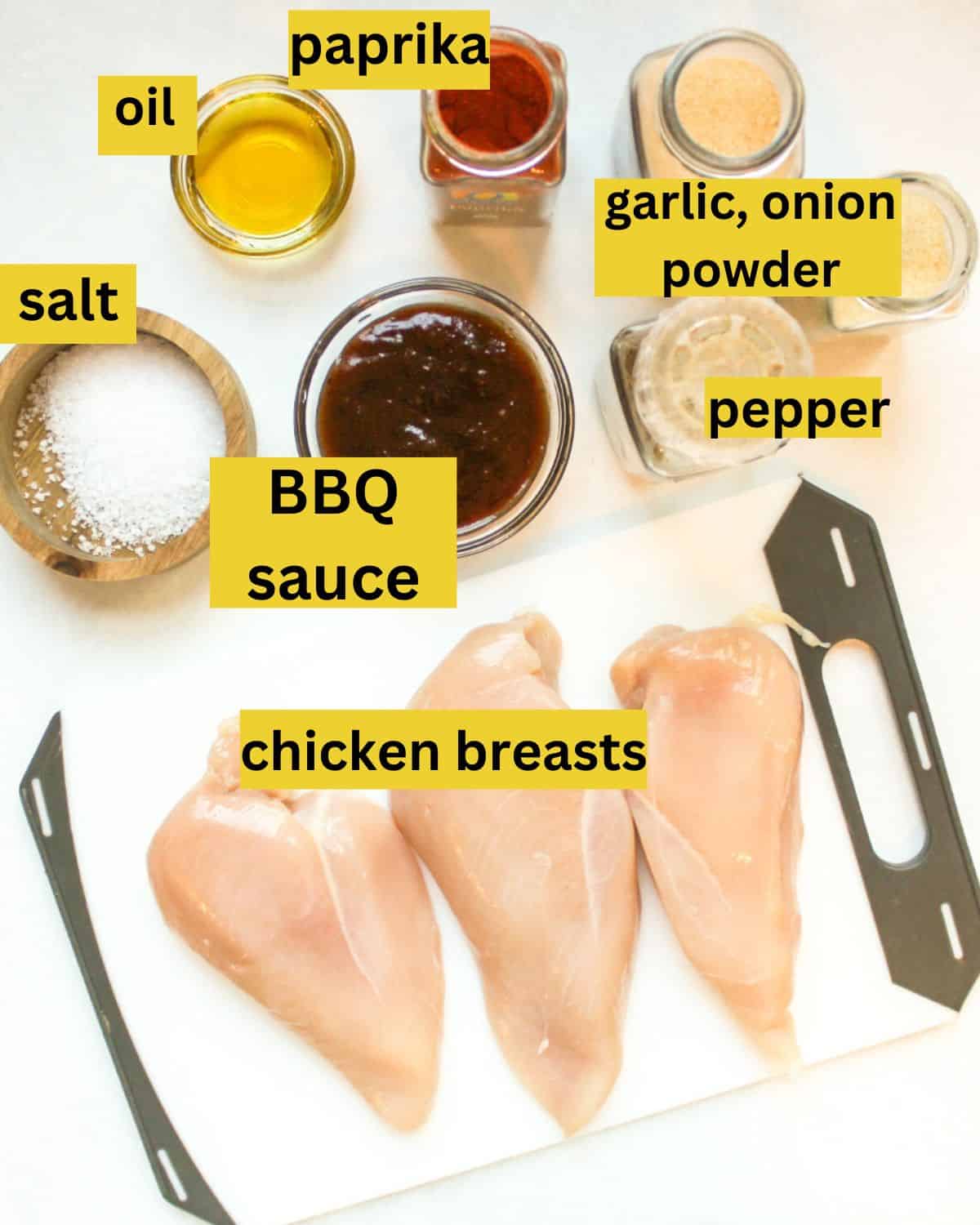 Recipe ingredients on a white background labeled as salt, BBQ sauce, chicken breasts, oil, paprika, garlic, onion powder, pepper.