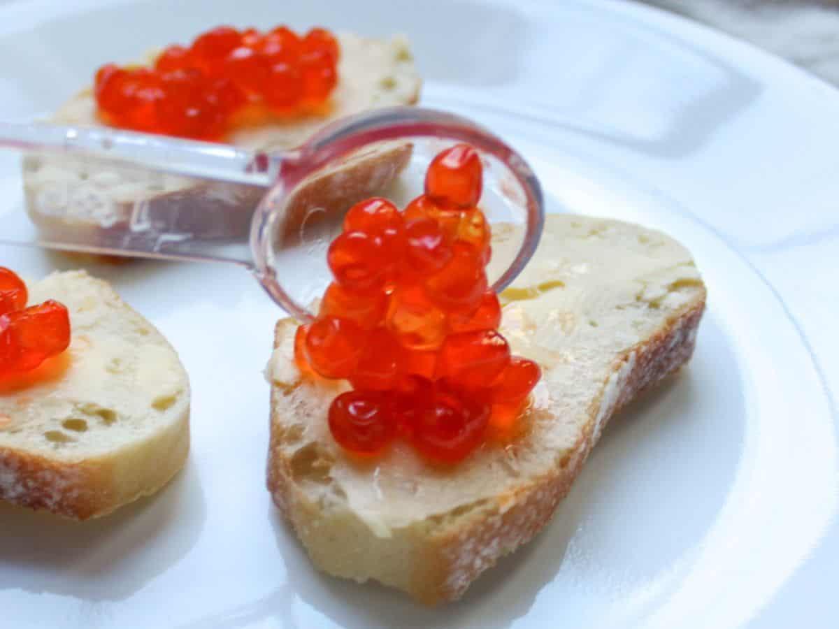 A spoonful of red salmon roe being added on top of the buttered bread slice.