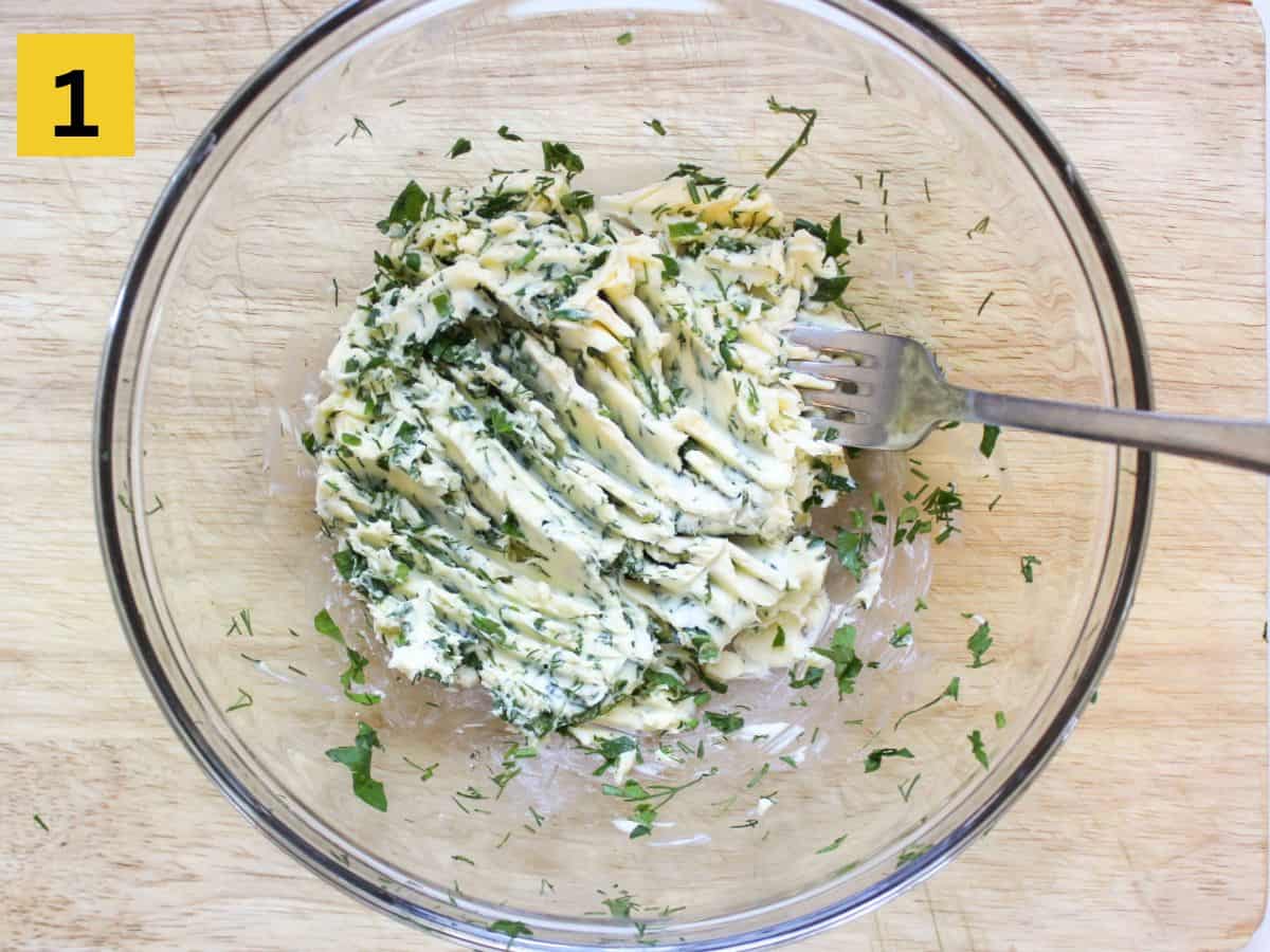 Softened butter mixed with fresh herbs in a glass bowl.