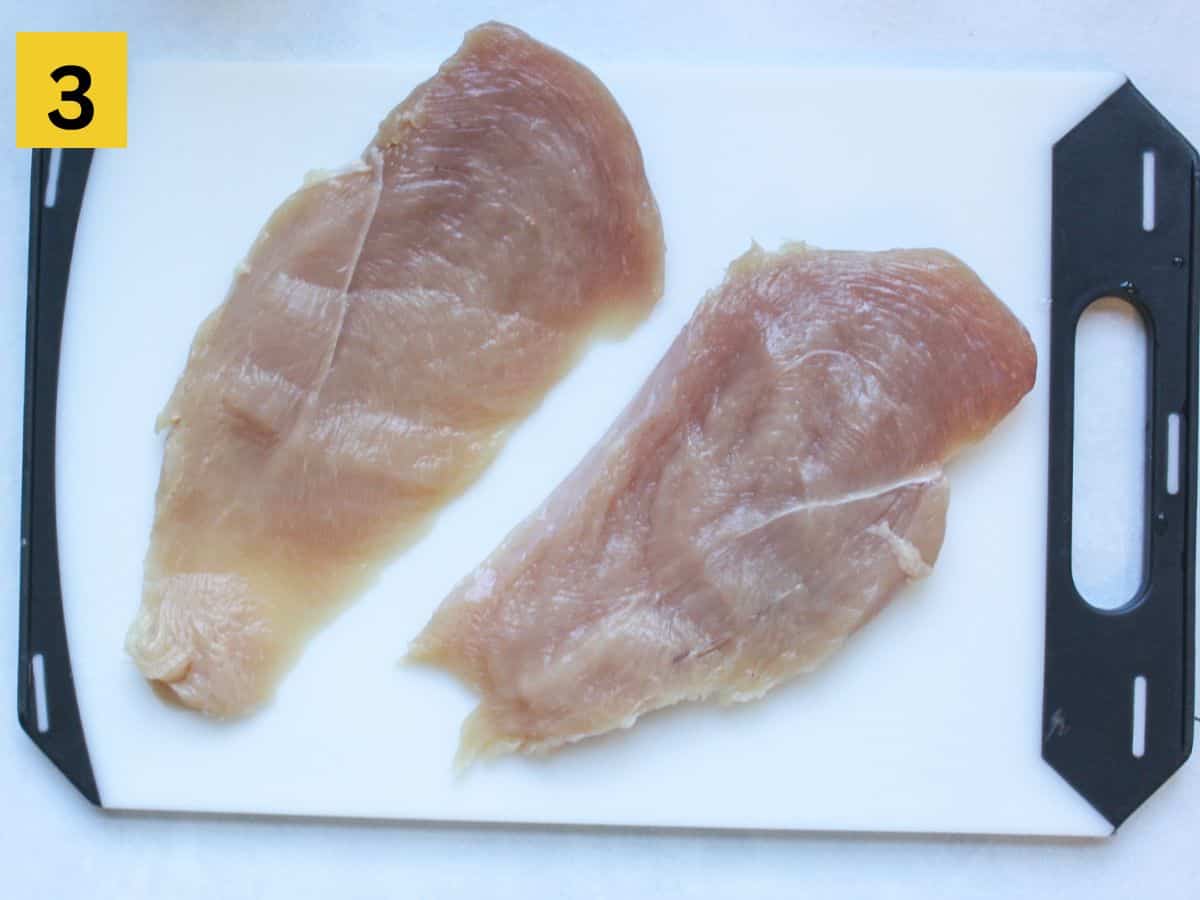 Two thinly sliced chicken cutlets on a white cutting board.