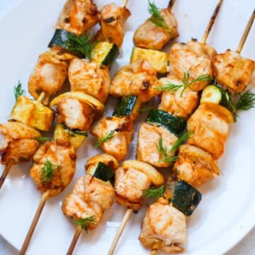 Baked chicken and vegges skewers on a white place garnished with fresh herbs on top.