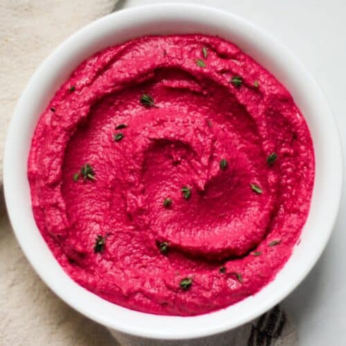 Pink beetroot hummus swirled in a white plate, elegantly garnished with green thyme leaves.