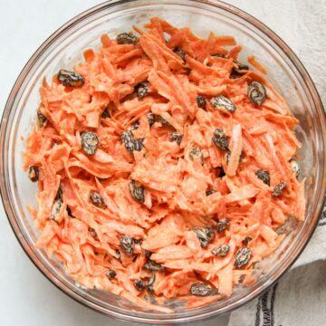 Carrots and raisin salad elegantly presented in a glass serving bowl.