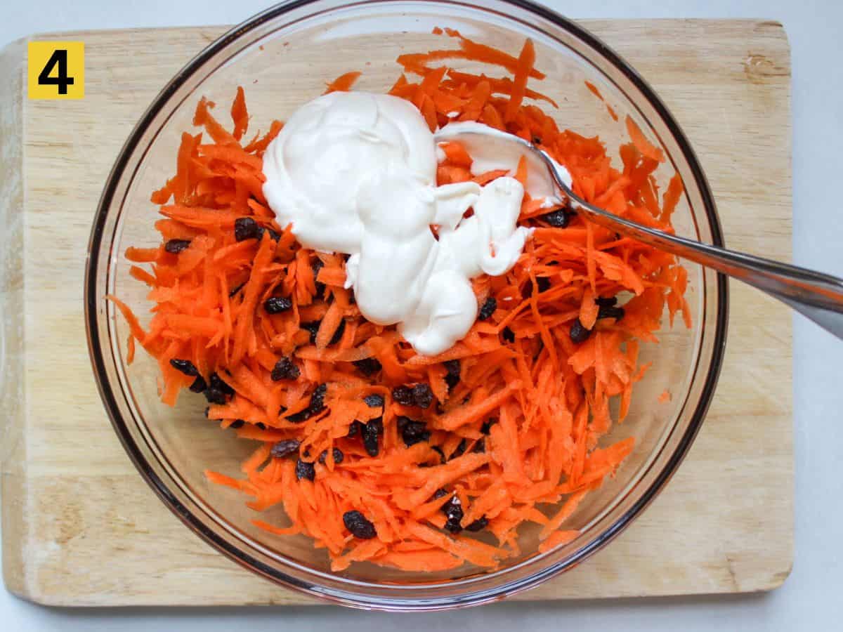 Mayo-based dressing being poured over a mix of grated carrots and raisins.