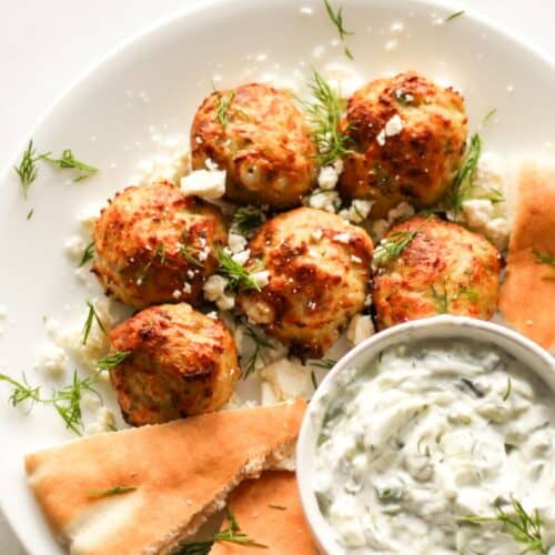 Greek chicken meatballs sprinkled with fresh dill on a white plate with pita bread and tzatziki sauce on the side.