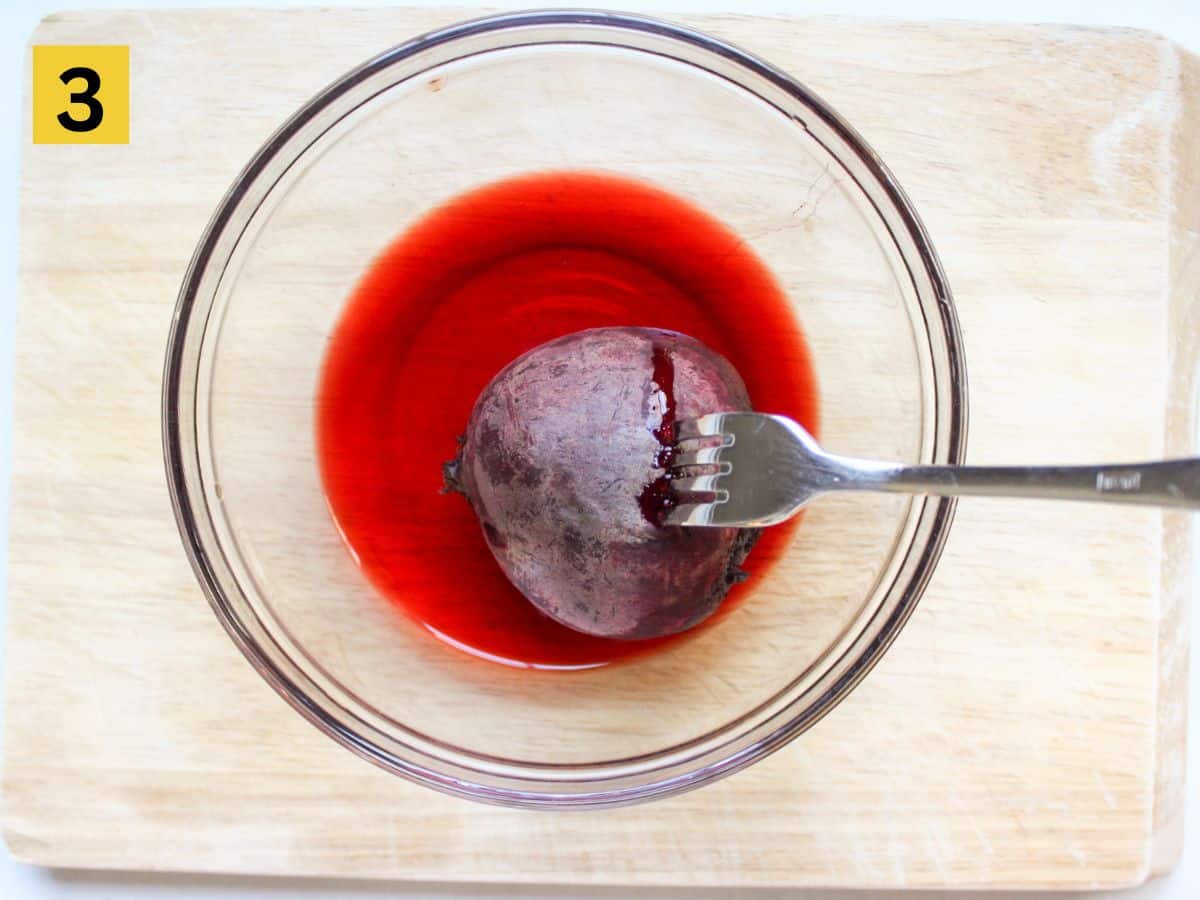 Cooked beetroot in a bowl with the fork pierced in it.