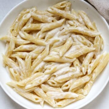 Penne pasta in a creamy cottage cheese sauce served in a white dish.