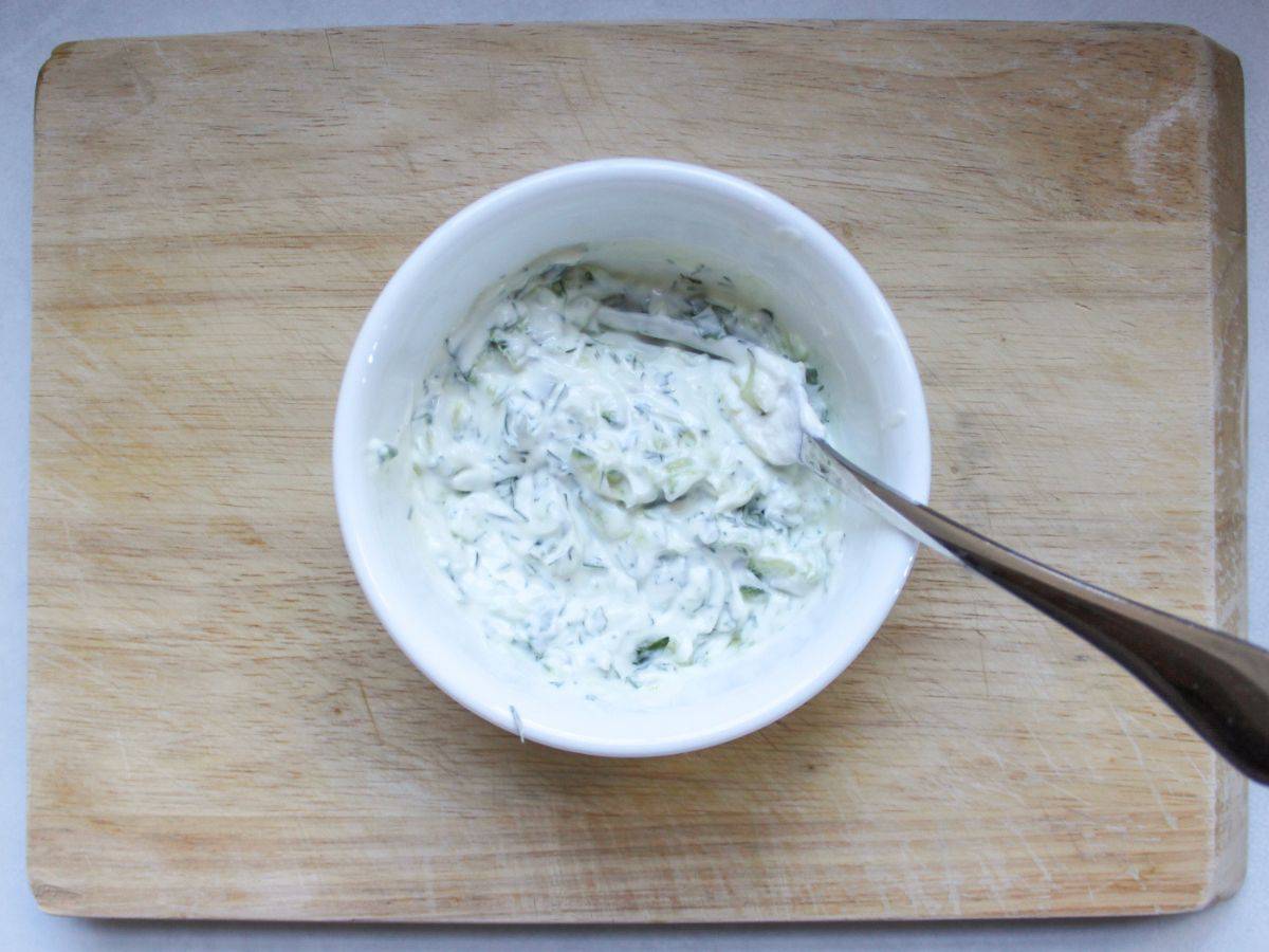 A small bowl with yogurt, cumber and herbs sauce.