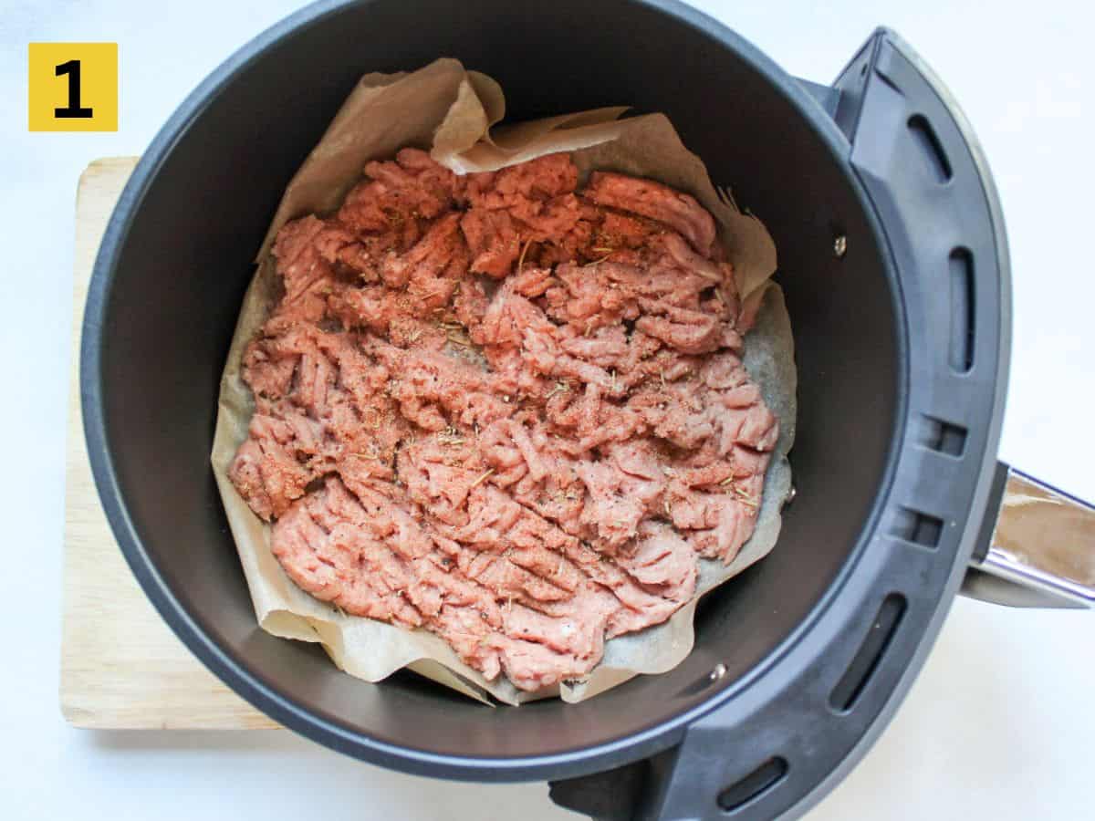 The initial recipe step of placing the uncooked ground turkey in the air fryer basket lined with parchment paper.