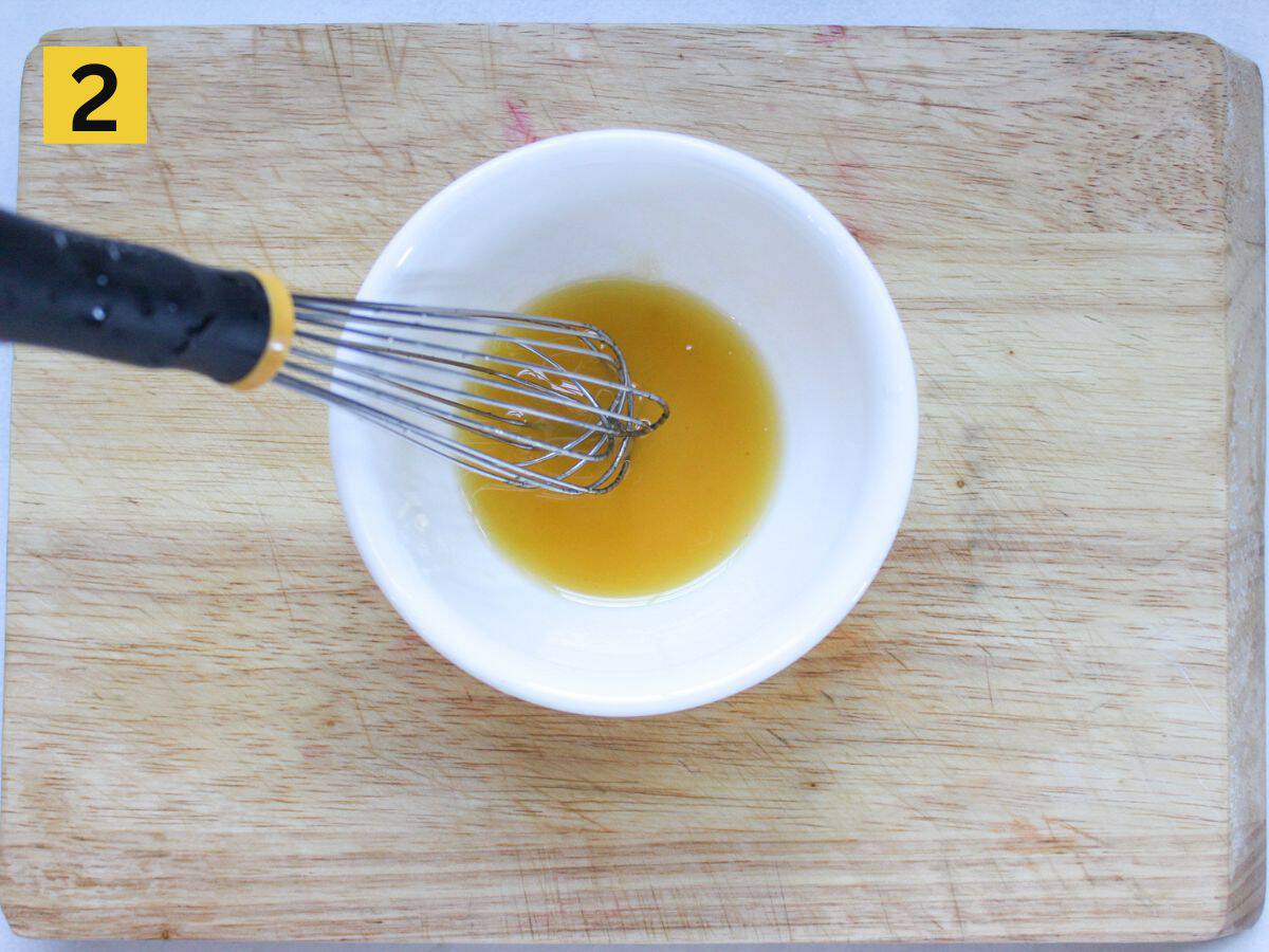 The whisk is blending yellow dressing in small white bowl