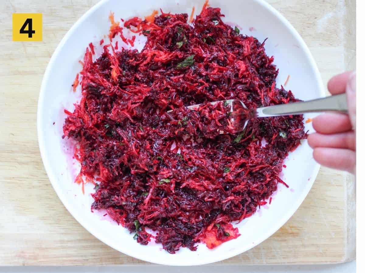 Grated beets, carrots and dressing in a white dish mixed with a fork.