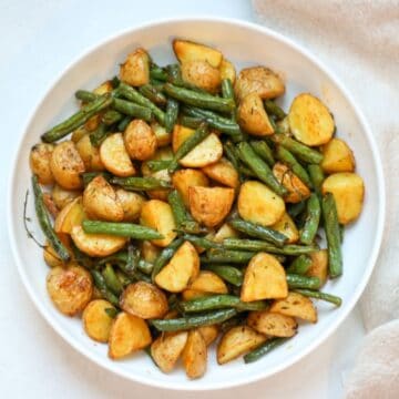 Roasted green beans and potatoes served in a white shallow dish.
