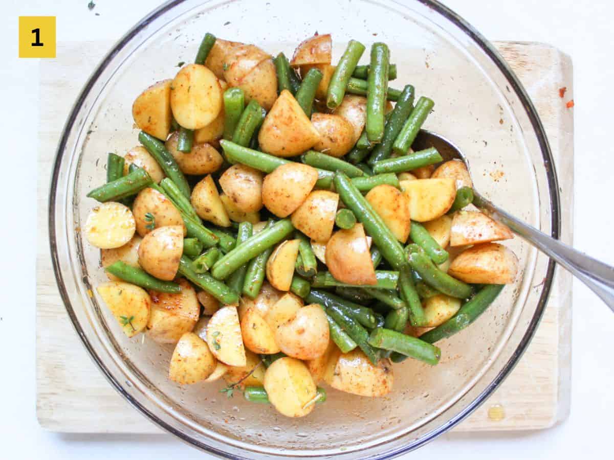 Chopped potatoes and green beans seasoned with olive oil and herbs in a glass mixing bowl