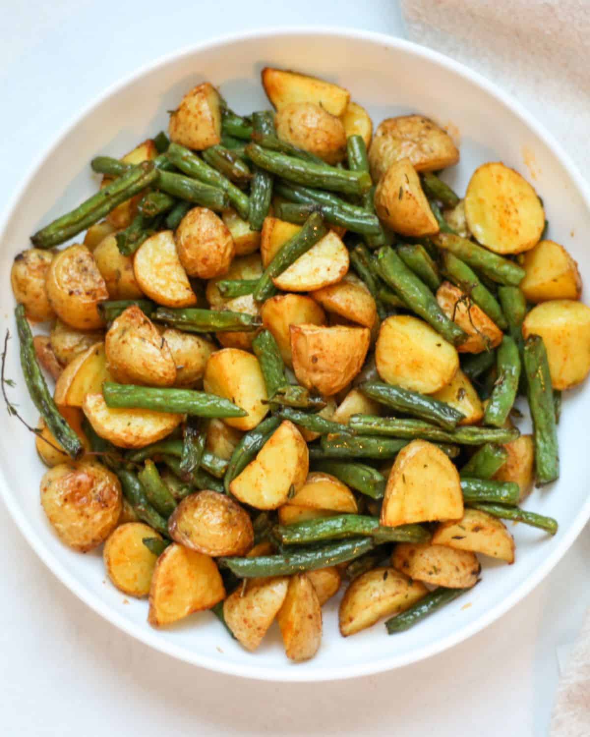 Roasted green beans and potatoes served in a white shallow dish. 