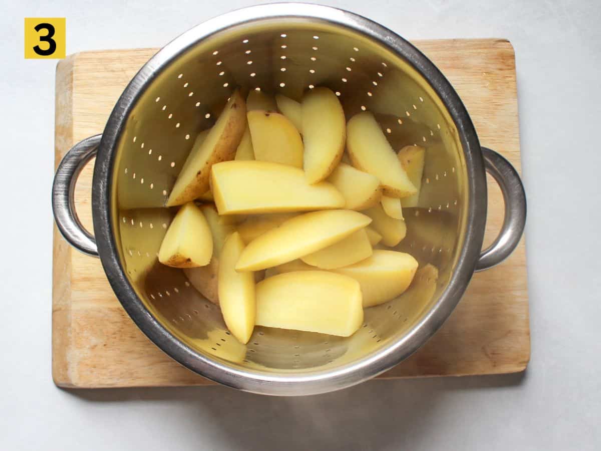 Parboiled potato wedges drying in a colander.