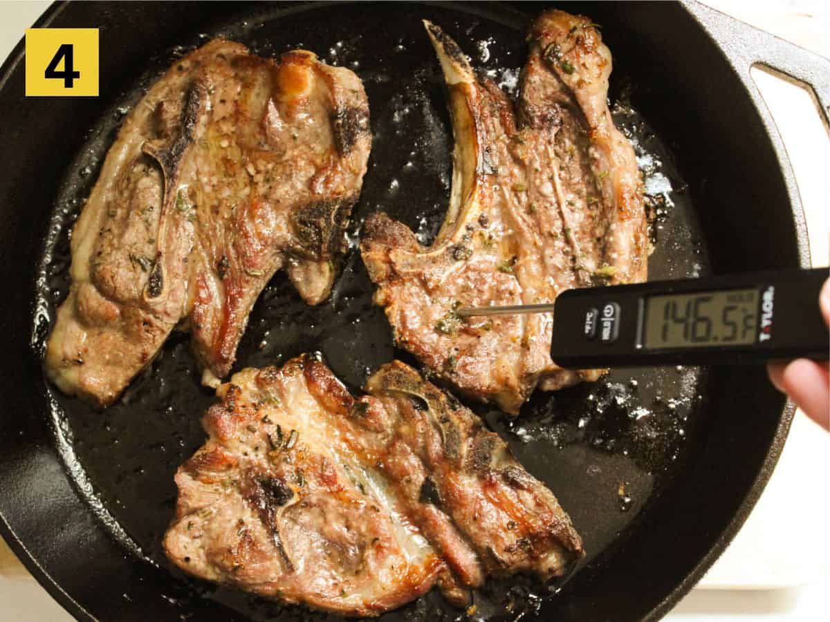 Cooked lamb chops sizzling on a skillet, one with a thermometer registering the temperature of 146°F.