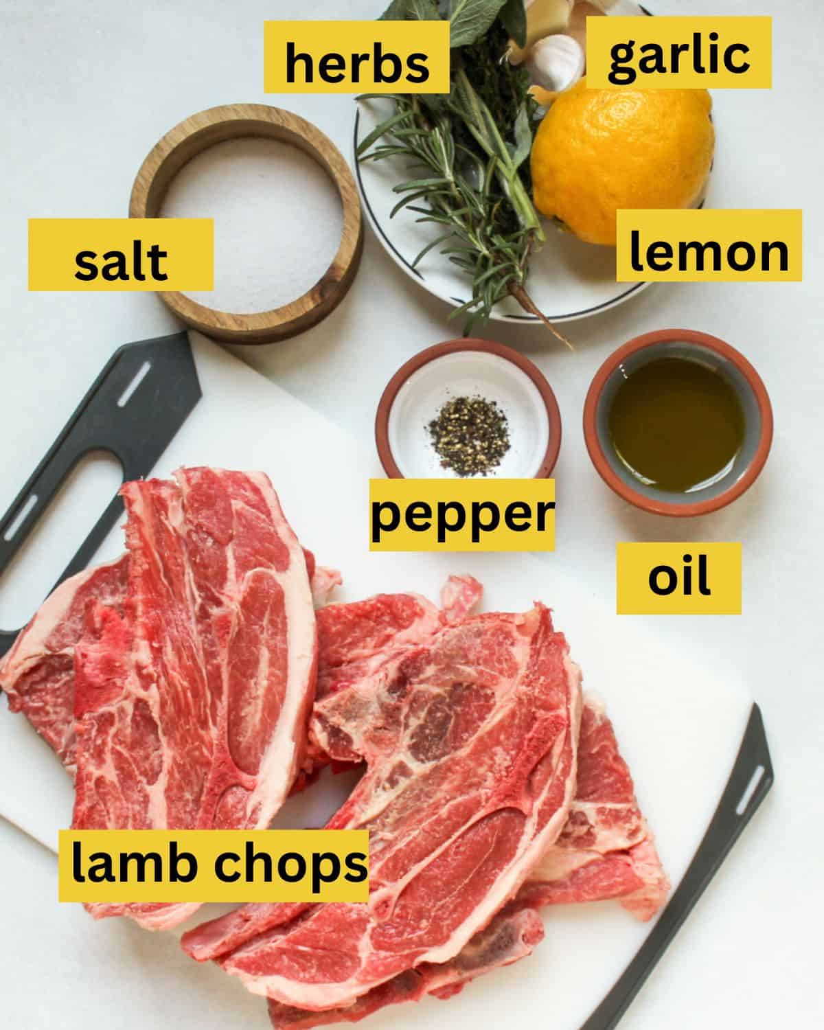 Recipe ingredients arranged on a white background and labeled as lamb chops, salt, herbs, garlic, lemon, pepper, oil.