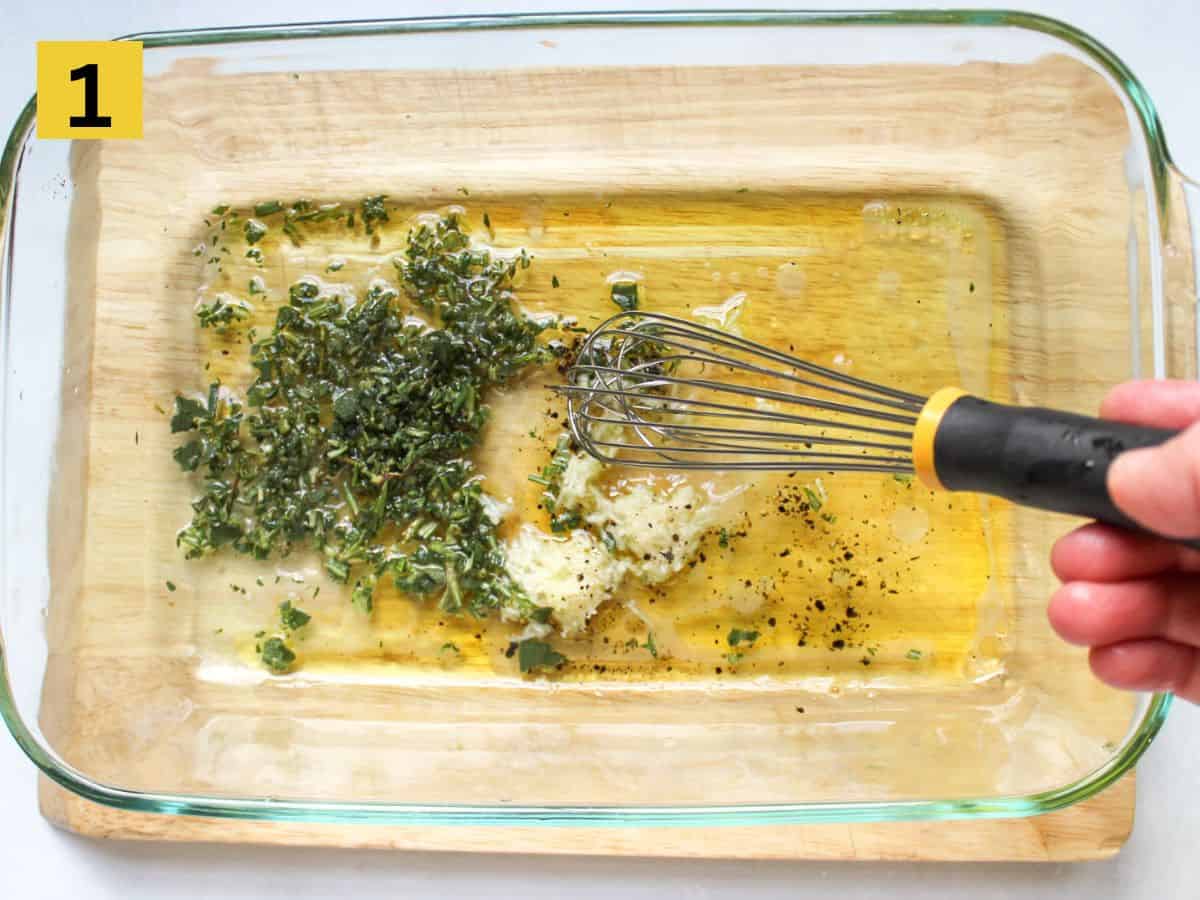 Glass container with oil, herbs and seasoning being mixed with a whisk.