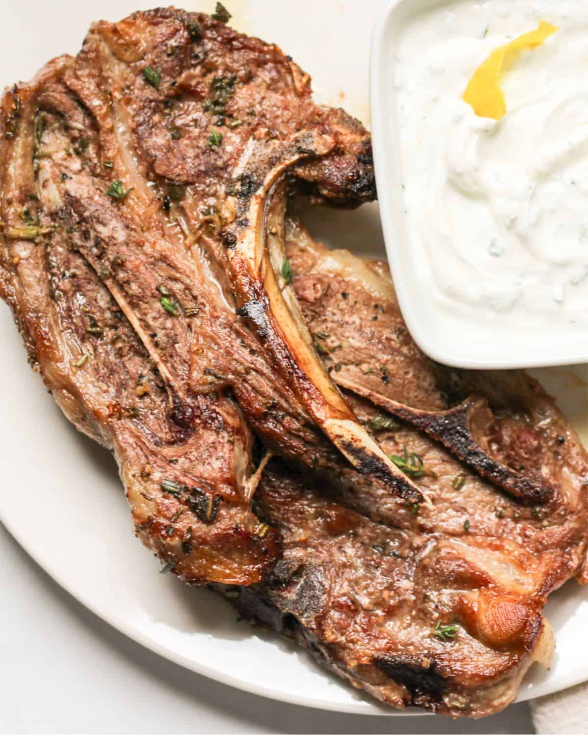 Cooked lamb served with a bowl of yogurt sauce on the side.