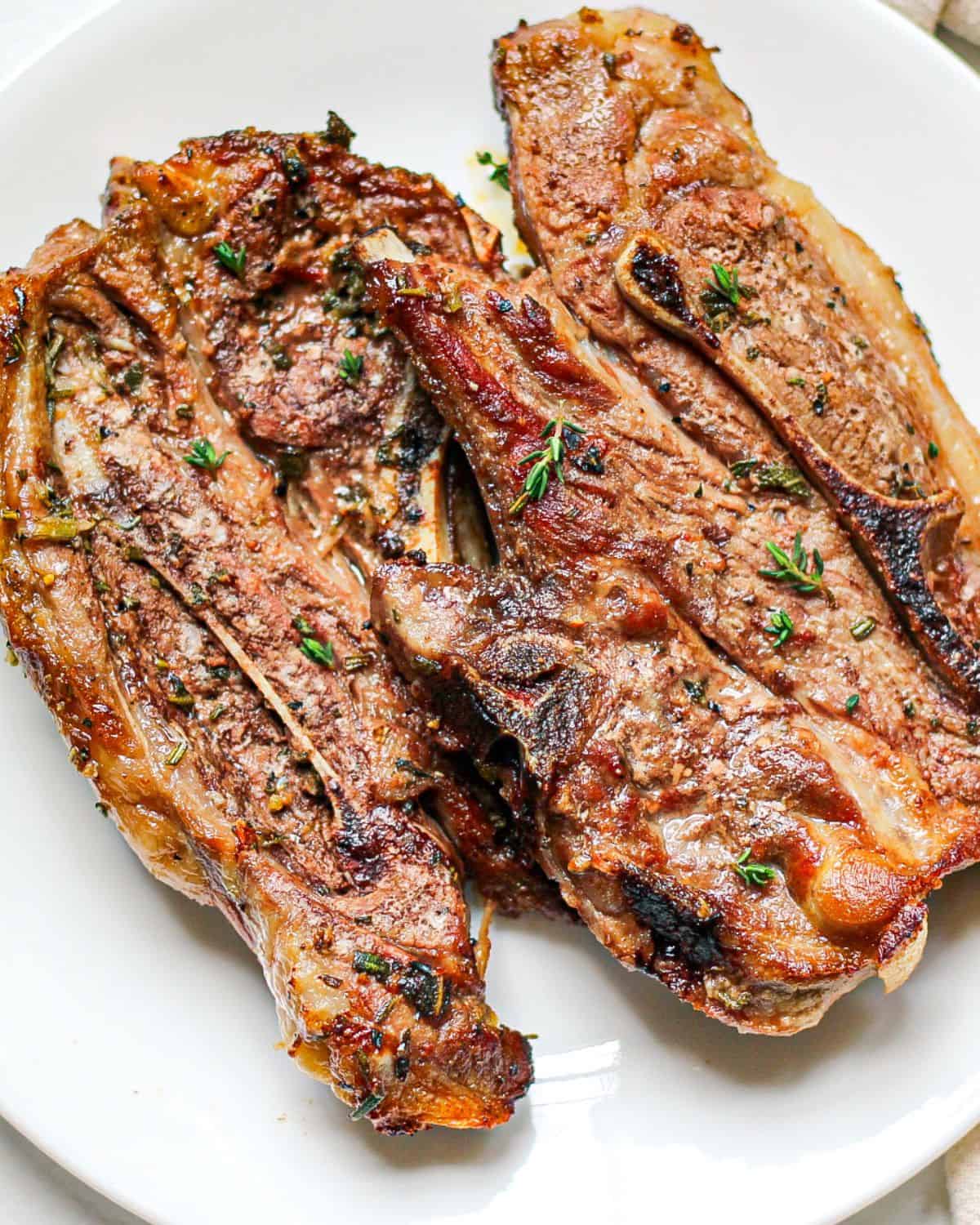 Perfectly baked lamb shoulder chops on a white plate garnished with green herbs on top. 