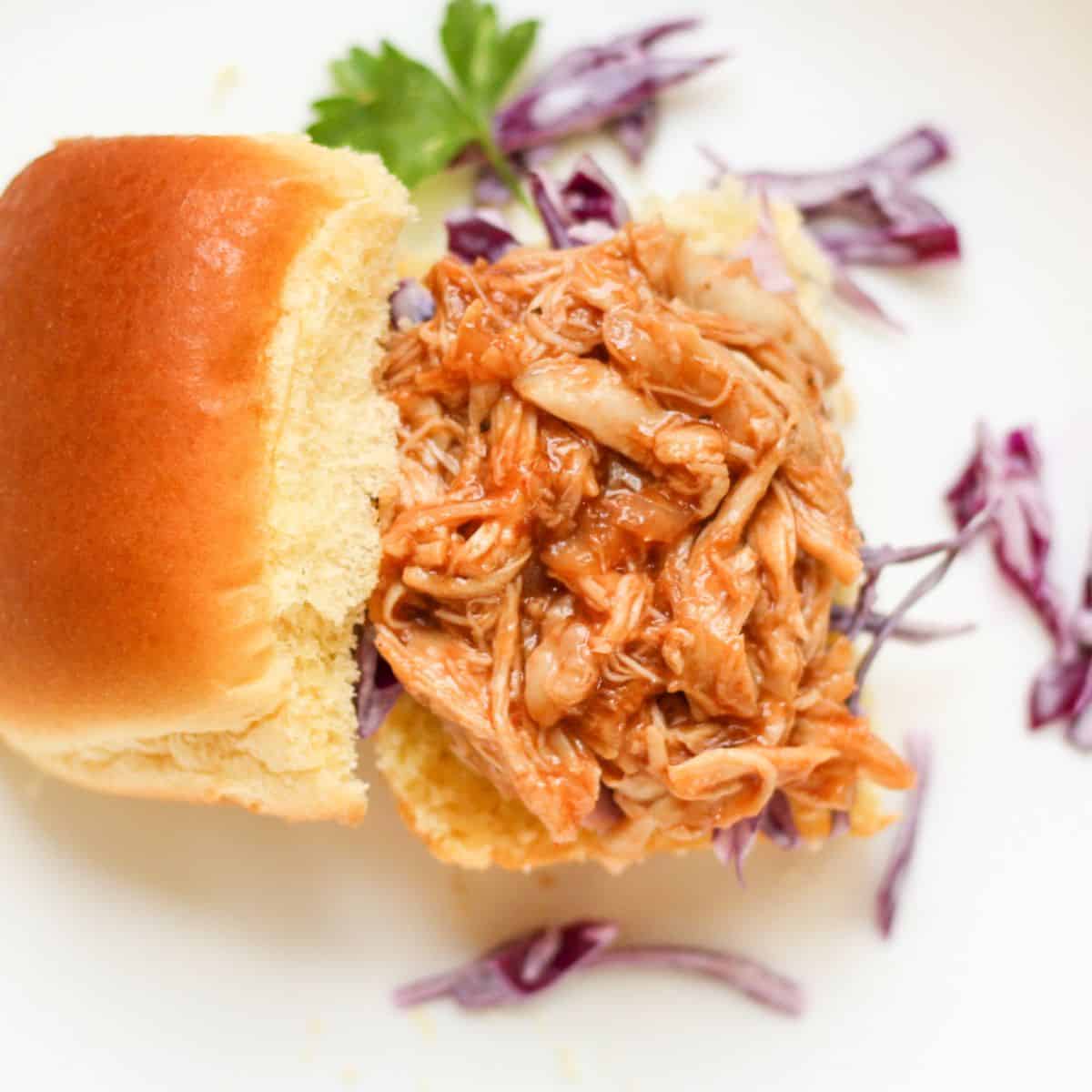 Instant Pot pulled BBQ chicken thighs piled on a sandwich bun with extra sauce.