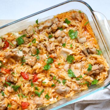 Baked chicken and orzo casserole garnished with chopped green herbs on top in a glass square dish.