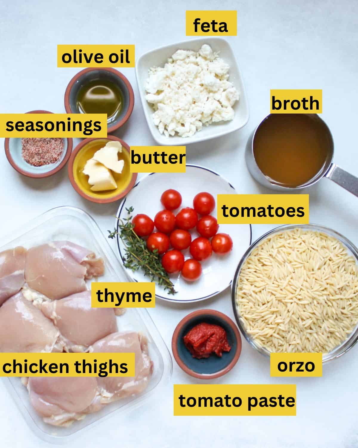 Recipe ingredients arranged in separate bowls and containers labeled as chicken thighs, seasonings, olive oil, butter, thyme, tomato paste, feta cheese. tomatoes, orzo, broth.