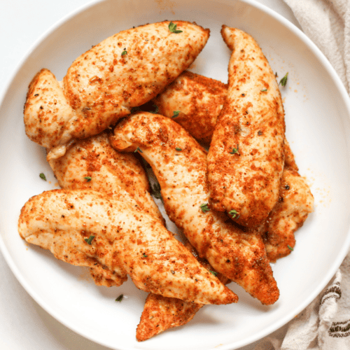 Oven baked chicken tenders without breading served on a white plate.