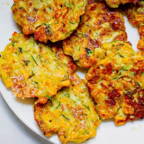 Golden brown zucchini and corn fritters served on a white dish.