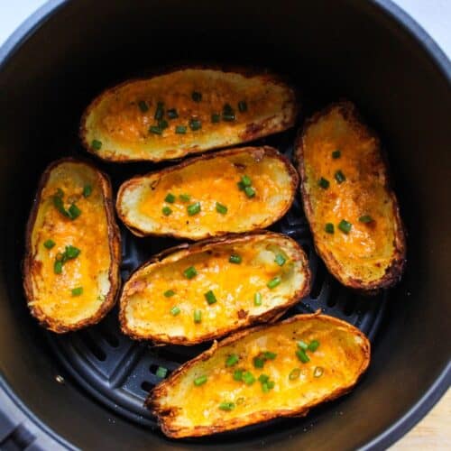 Crispy potato skins with melted cheese in the air fryer basket.