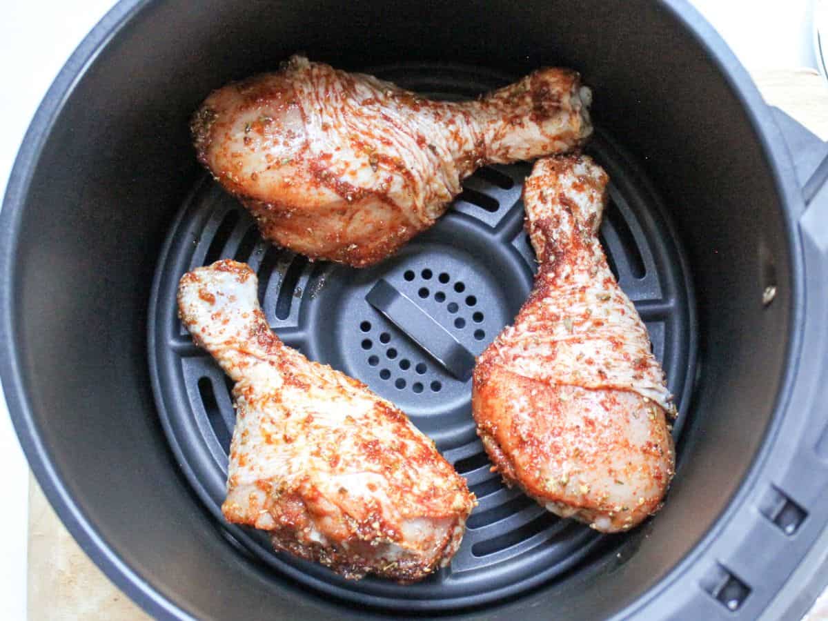 Chicken drumsticks arranged in air fryer basket before cooking.