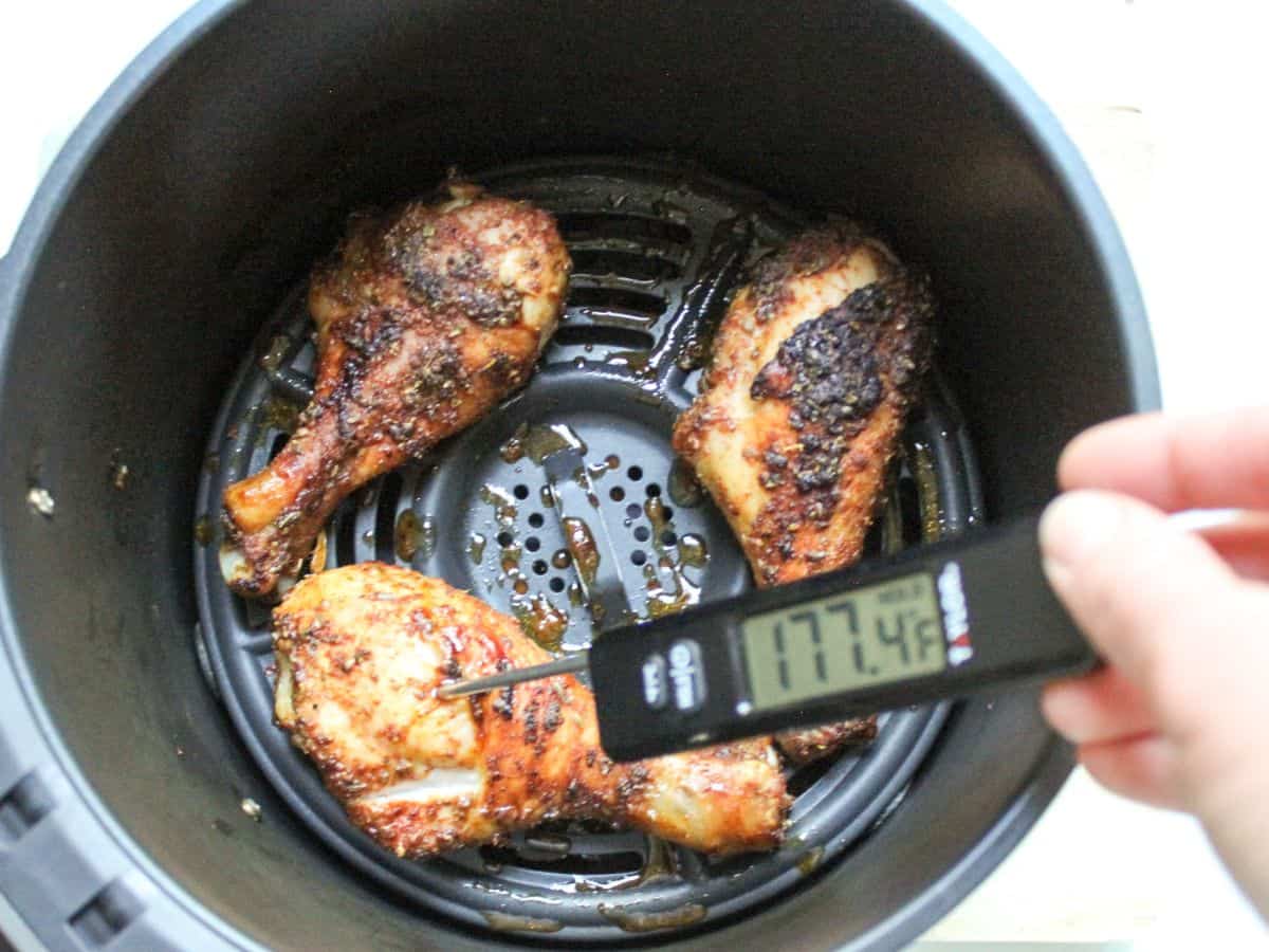 Crispy chicken drumsticks in air fryer basket, with a meat thermometer inserted in one of the drumsticks.