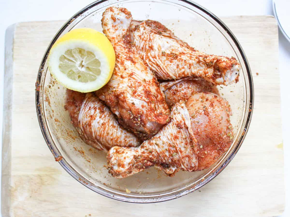 Seasoned raw chicken drumsticks in a glass bowl. 