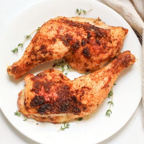Two roasted chicken leg quarters with crispy skin served on a white dish.