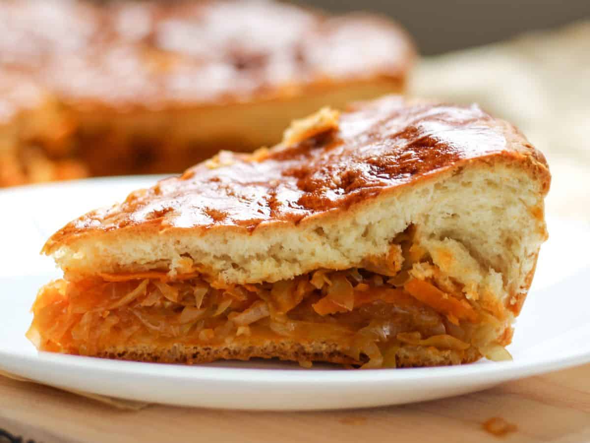 A slice of savory pie with cabbage filling served on a white plate.
