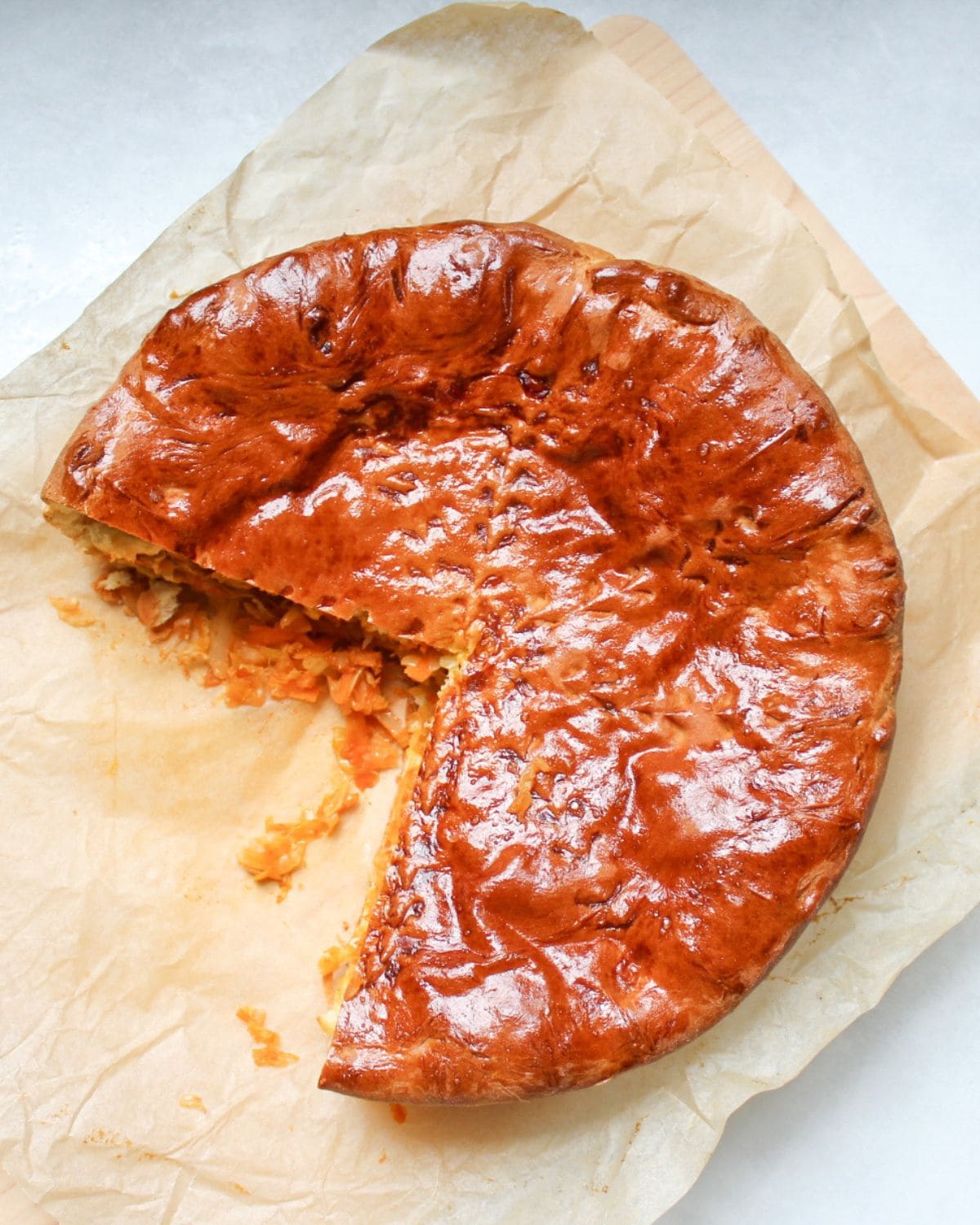 A large, golden-brown cabbage pie on parchment paper with one slice removed, revealing its savory cabbage filling.