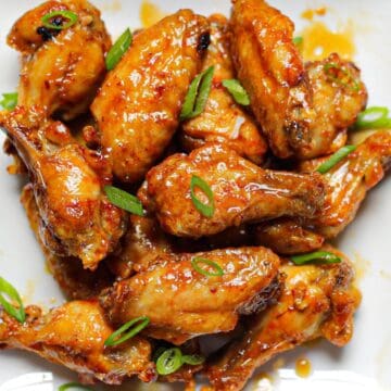 Air fried chicken wings coated in a sticky honey garlic sauce and topped with thinly sliced green onion on a plate.