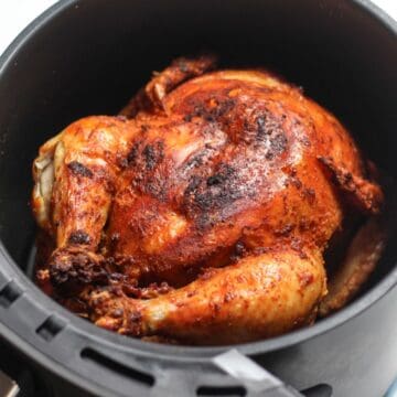 Roasted whole chicken with golden skin in air fryer basket