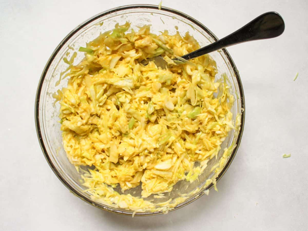 Cabbage fritters batter in a large glass bowl with a fork in it.