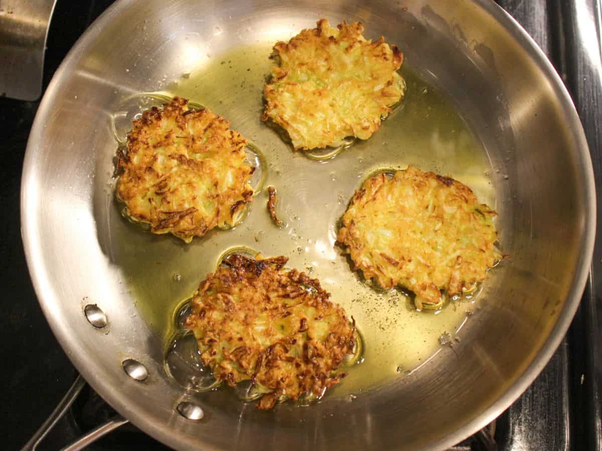 Golden brown cabbage fritters sizzling in a frying pan.