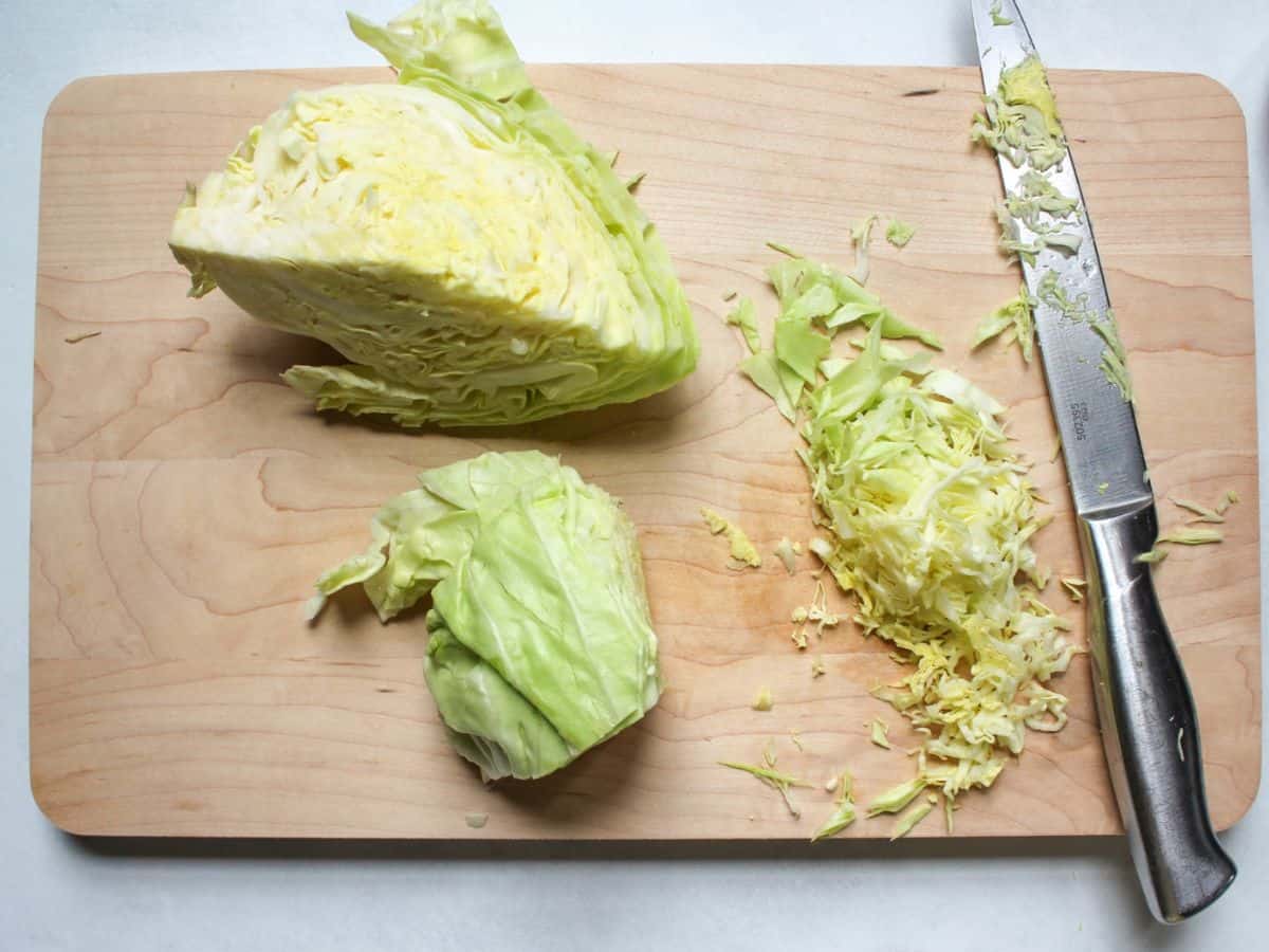 Shredding cabbage with a knife on a wooden cutting board into thin shreds.