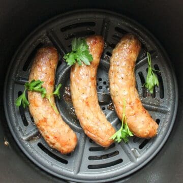 Three golden-brown air-fried bratwursts in air fryer basket.