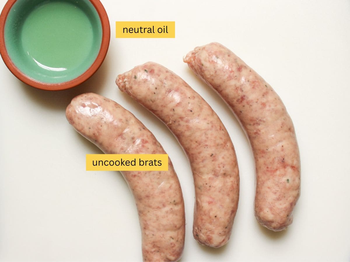 Uncooked bratwursts and a small bowl with oil on a white surface.