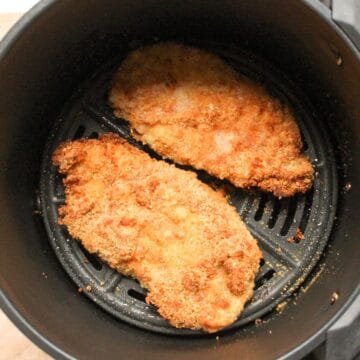 Crispy golden chicken schnitzels in air fryer basket.