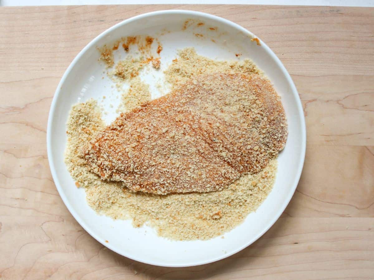 Chicken is coated in breadcrumbs in a shallow dish.