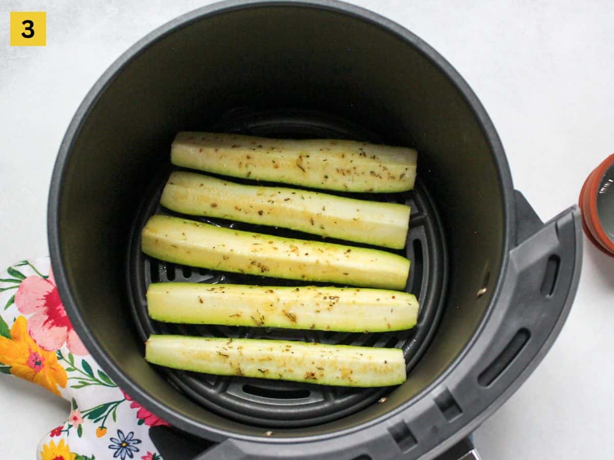Seasoned zucchini arranged in air fryer basket in a single layer.